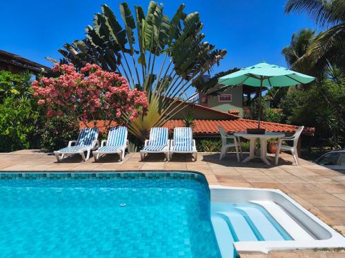 a swimming pool with chairs and a table and an umbrella at Pousada Casa Franco - Trancoso in Trancoso