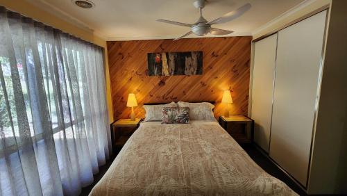 a bedroom with a bed with two lamps and a ceiling fan at Ellimata Holiday Cottage in Halls Gap