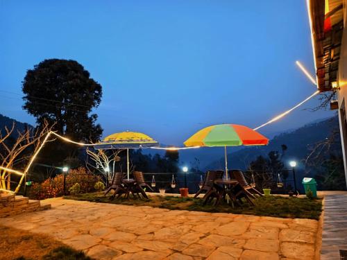 deux parasols et des chaises assis sur une terrasse la nuit dans l'établissement A Home Above the Clouds Riturain Mukteshwar, à Mukteswar