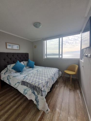 a bedroom with a bed with blue pillows and a chair at Departamento full equipado in Coquimbo
