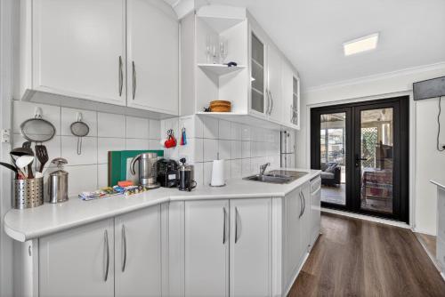 a white kitchen with white cabinets and wooden floors at Coastal 2-Bed Home with Pool in Safety Bay