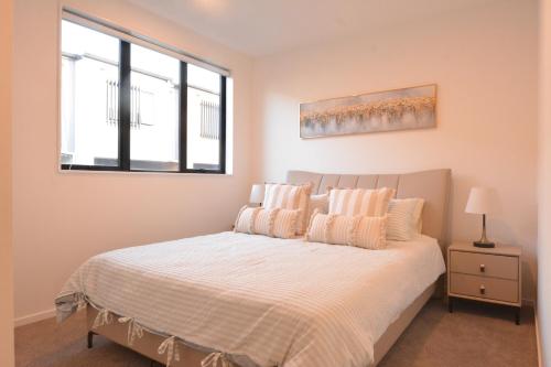 a bedroom with a bed with two pillows and a window at Modern 3BR Family Townhouse & Walk to Train & Free Parking & Gated Community in Auckland