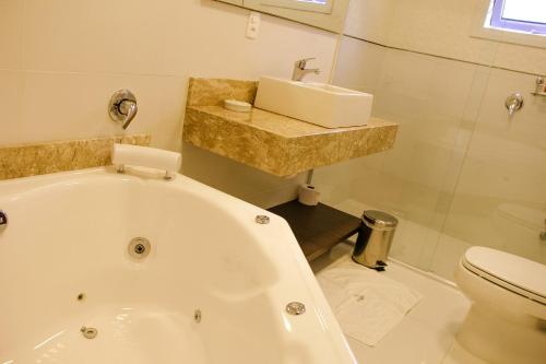a bathroom with a tub and a sink and a toilet at Hotel Gramado Interlaken in Gramado
