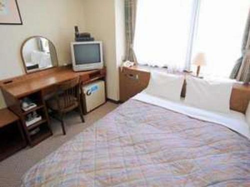 a bedroom with a bed and a desk and a television at Hotel Crown Hills Matsuyama in Matsuyama
