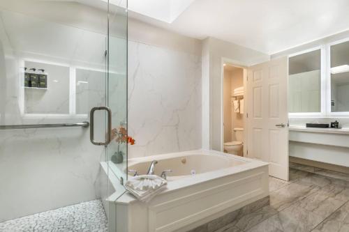 ein weißes Badezimmer mit Badewanne und Dusche in der Unterkunft University Park Inn & Suites, an Ascend Collection Hotel in Davis