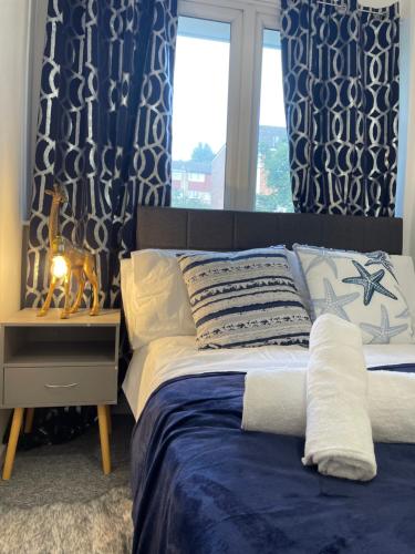 a bedroom with a bed with blue curtains and a window at Skyway Suites Luton in Luton