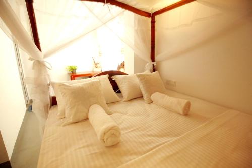 a bed with white pillows in a room with a window at Kandy House Hiriketiya in Dickwella
