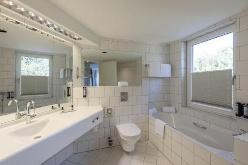 a bathroom with a sink and a toilet and a tub at ARCOTEL Kaiserwasser Wien in Vienna