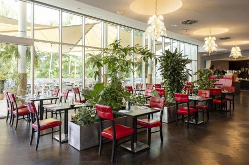 a restaurant with tables and red chairs and plants at ARCOTEL Kaiserwasser Wien in Vienna