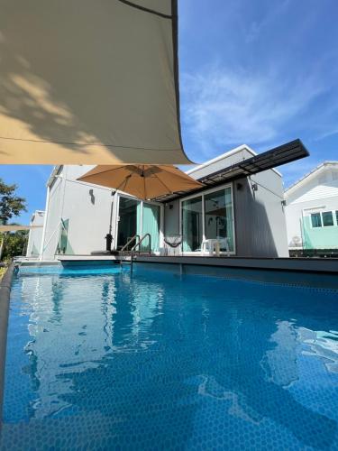 een zwembad met parasol naast een huis bij Home stay Ev Coffeehouse in Ban Map Khao Wan