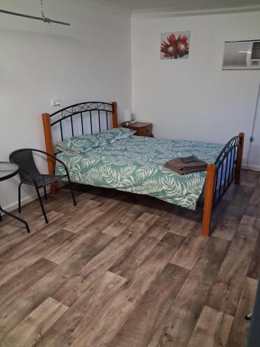 a bedroom with a bed and a chair and wooden floors at Cartledge Ave studio and house homestay in Whyalla