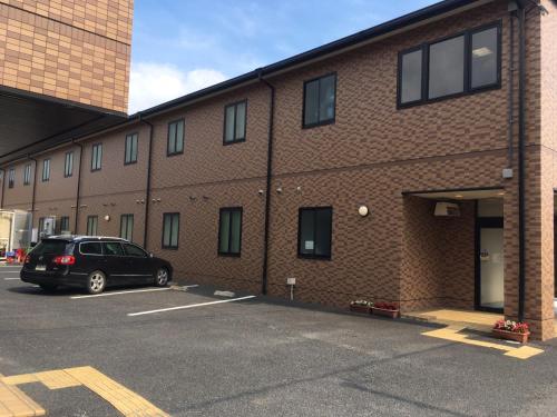 a car parked in a parking lot next to a brick building at Hotel Tajimi Hills Myroom in Tajimi