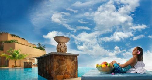 a woman sitting next to a bowl of fruit next to a pool at PULSE GRANDE Hotel Putrajaya in Putrajaya