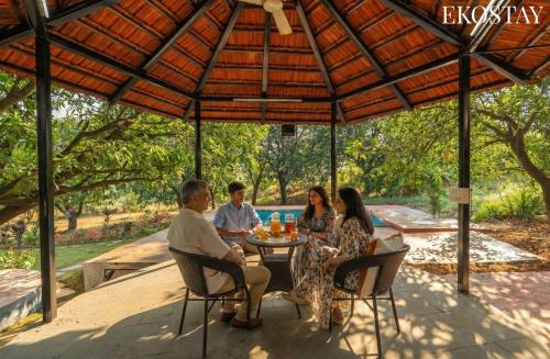 a group of people sitting at a table under an umbrella at EKOSTAY - Brick Wood in Karjat