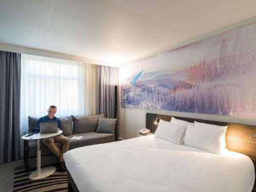 een man in een hotelkamer met een laptop bij Novotel Lyon Bron Meeting & Events in Bron