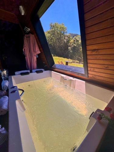 a bathtub in a room with a large window at Chalé Aconchego Alfredo Wagner in Alfredo Wagner