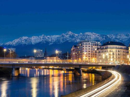 a bridge over a river with buildings and snow covered mountains at ibis Grenoble Gare in Grenoble