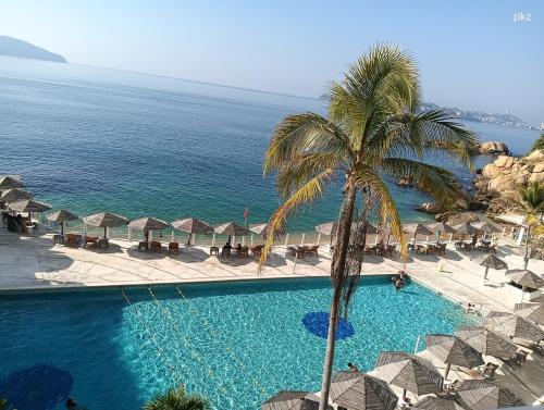 a swimming pool with a palm tree and the ocean at SUITE TORRES GEMELAS 2902 vista al mar in Acapulco