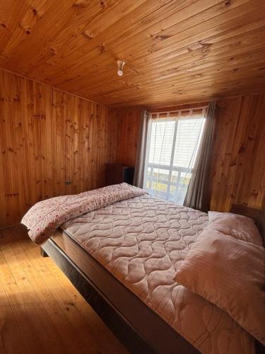 een bed in een houten kamer met een raam bij Cabañas Vitalis in Curanipe