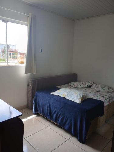 a bedroom with a bed with blue sheets and a window at Residencial Daitx in Capão da Canoa