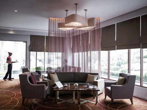 een vrouw die in een lobby staat met een bank en stoelen bij Pullman Hanoi in Hanoi