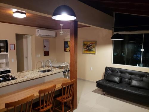 een woonkamer met een zwarte leren bank en een keuken bij Condomínio Jardins in Garopaba
