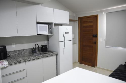 eine Küche mit weißen Schränken und einem weißen Kühlschrank in der Unterkunft Loft 01 dormitório in Tubarão