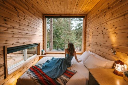 a woman sitting on a bed in a room with a window at Postcard Cabins Big Bear, Outdoor Collection by Marriott Bonvoy in Running Springs