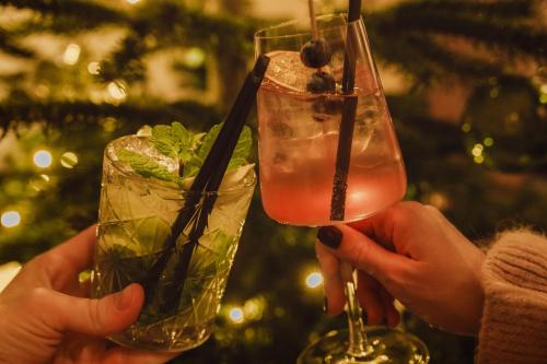 due persone che tengono in mano due cocktail davanti a un albero di Natale di Hotel Bad Fallenbach a San Leonardo in Passiria