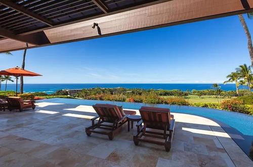 a patio with chairs and a pool and the ocean at Luxury Oceanview Villa with Infinity Pool in Hapuna Beach