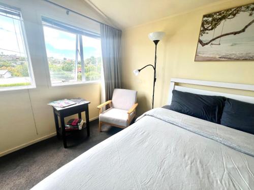 a bedroom with a bed and a chair and a lamp at Cosy Retreat Near Mairangi Bay in Auckland