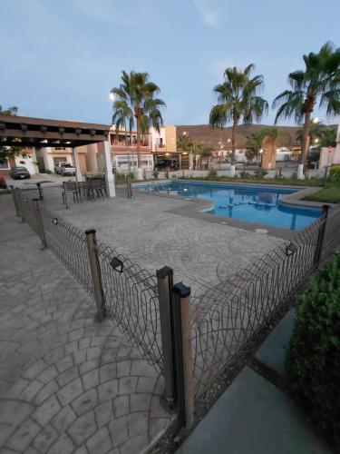 a fence in front of a swimming pool with palm trees at Casa en condominio Mediterráneo in La Paz