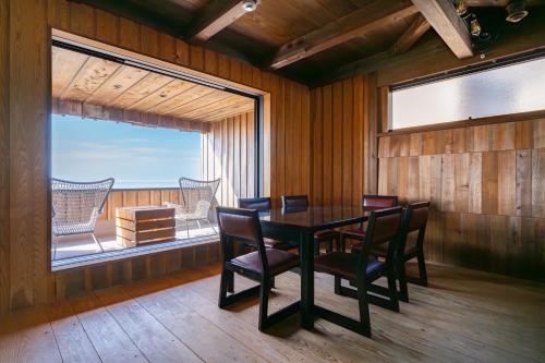 een eetkamer met een tafel en stoelen en een groot raam bij マーレゲストハウス in Fukui