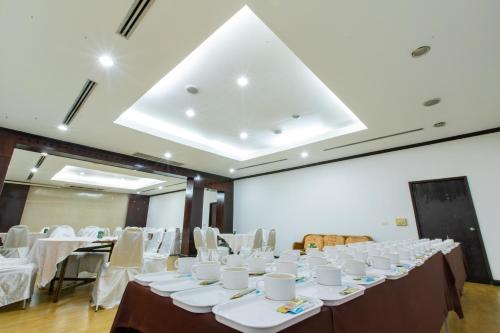 een kamer met witte tafels en stoelen en een hoog plafond bij Royal Diamond Hotel in Phetchaburi