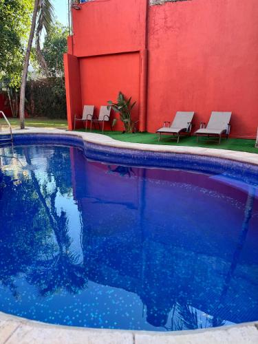 a swimming pool with two chairs and a red wall at Casa Arcángel SM in Cruz de Huanacaxtle