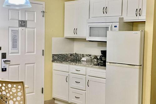 a kitchen with white cabinets and a white refrigerator at Suburban Studios Fort Myers Cape Coral in Fort Myers