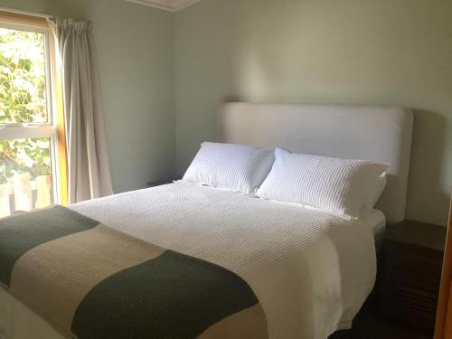 a bedroom with a bed with white sheets and a window at Ocean Breeze Holiday Home in Riverton