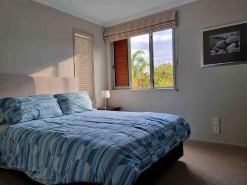 a bedroom with a bed with a blue comforter and a window at Villa 46 in Pauanui