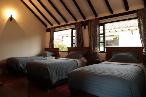 two beds in a room with two windows at Finca Villa Sofía in Villa de Leyva