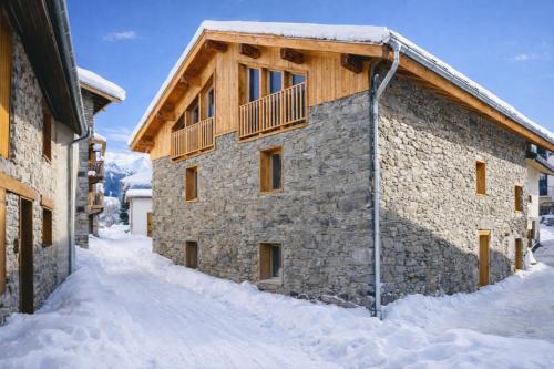un bâtiment en pierre dans la neige avec un balcon dans l'établissement Les Framboisiers by Lodji, à Saint-Marcel