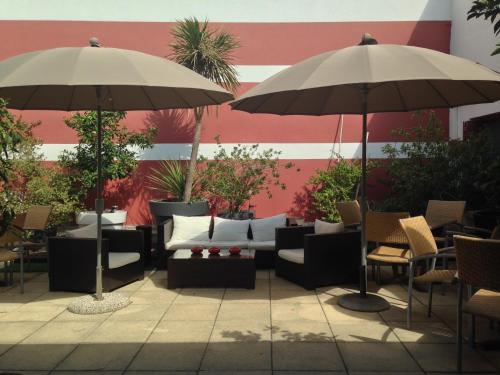 un patio con sofás, mesas y sombrillas en Hotel Cote Patio en Nimes