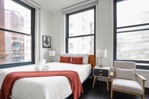 a bedroom with two beds and a chair and windows at CozySuites at William in Pittsburgh