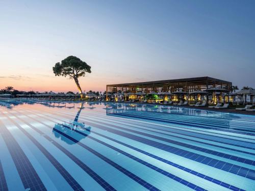 een groot zwembad met een boom en een gebouw bij Rixos Premium Belek - The Land of Legends Access in Belek