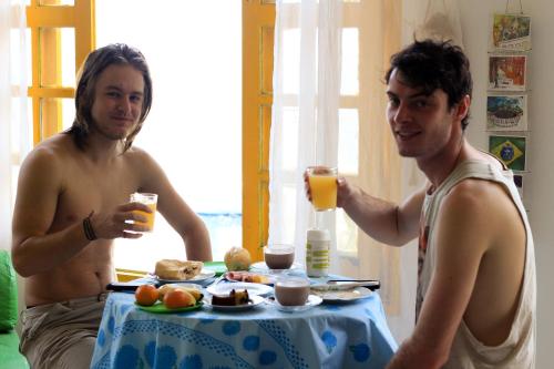 Zwei Männer sitzen an einem Tisch und trinken Orangensaft. in der Unterkunft Mar da Babilônia Hostel in Rio de Janeiro