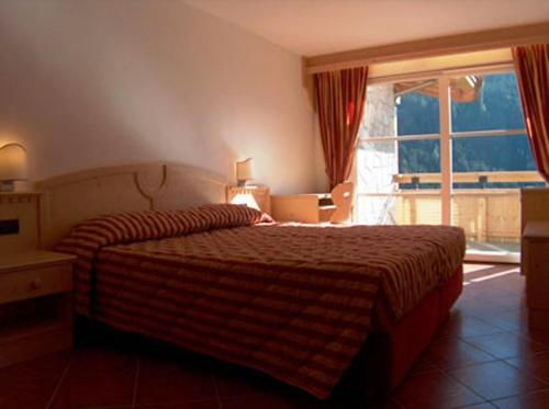 um quarto de hotel com uma cama e uma grande janela em Residence Club La Betulla em Pozza di Fassa