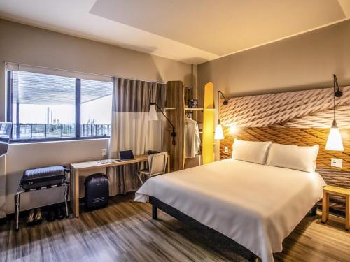 a hotel room with a bed and a desk and a window at ibis Palmas Avenida JK in Palmas