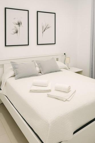 a white bed with three pictures on the wall at Alojamiento Baeza California 2B in Baeza