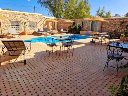 un patio con tavoli e sedie accanto a una piscina di Villa Nouran - Chambre Hôte a Ghazoua
