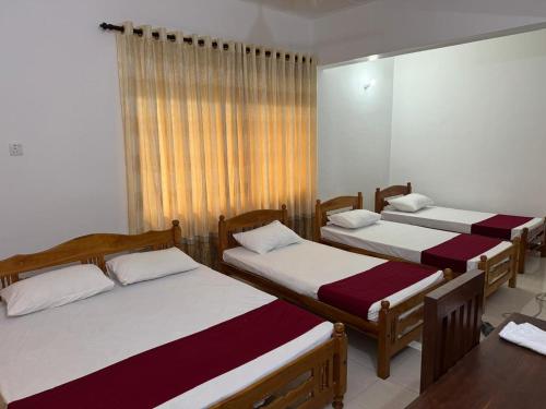 een kamer met drie bedden en een tafel bij Vinola Hotel in Mannar