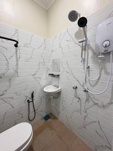 a white bathroom with a toilet and a sink at Sasuka Inn Rusila in Marang